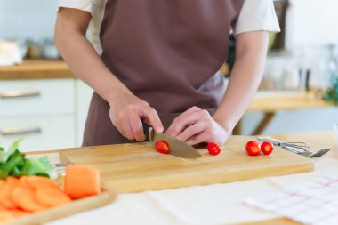 Asyalı kadınlar domatesleri bıçakla doğrayarak kahvaltı hazırlamak için taze sebze hazırlarken aynı zamanda evde, mutfakta sağlıklı bir yaşam tarzı hazırlıyorlar..