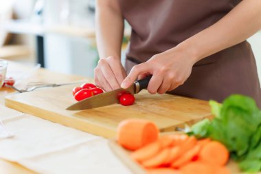 Asyalı kadınlar domatesleri bıçakla doğrayarak kahvaltı hazırlamak için taze sebze hazırlarken aynı zamanda evde, mutfakta sağlıklı bir yaşam tarzı hazırlıyorlar..