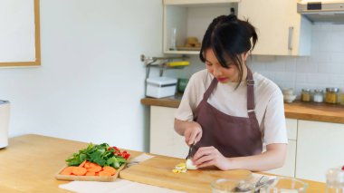 Asyalı kadınlar kaynatılmış yumurtayı panoda bıçakla kesiyorlar ve kahvaltı hazırlamak için taze sebzeleri dilimliyorlar. Evde, mutfakta sağlıklı yiyecek yaşam tarzları hazırlıyorlar..