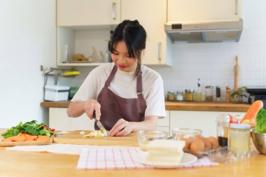Asyalı kadınlar kaynamış yumurtayı panoda bıçakla doğruyor ve kahvaltı hazırlamak için taze sebzeleri dilimlerken aynı zamanda evdeki mutfakta sağlıklı yiyecek yaşam tarzları hazırlıyorlar..