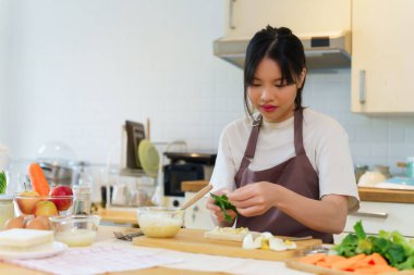 Asyalı kadınlar ekmeğin üzerine haşlanmış yumurta salatası ve sebze koyarken aynı zamanda kahvaltı hazırlamak ve evdeki mutfakta sağlıklı yemek yapmak için malzemeler hazırlıyorlar..