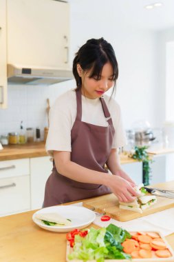 Asyalı kadınlar sebzeli ve mayonezli lezzetli sandviçler yapıyorlar. Kahvaltıda yemek pişirirken bıçakla sandviç dilimlemek ve mutfakta sağlıklı yemek yapmak için..