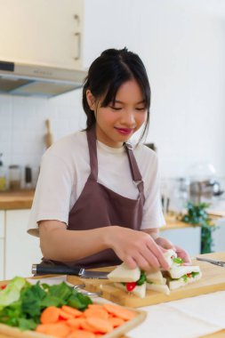 Asyalı kadınlar sebzeli ve mayonezli lezzetli sandviçler yapıyorlar. Kahvaltıda yemek pişirirken bıçakla sandviç dilimlemek ve mutfakta sağlıklı yemek yapmak için..