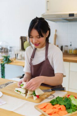 Asyalı kadınlar sebzeli ve mayonezli lezzetli sandviçler yapıyorlar. Kahvaltıda yemek pişirirken bıçakla sandviç dilimlemek ve mutfakta sağlıklı yemek yapmak için..