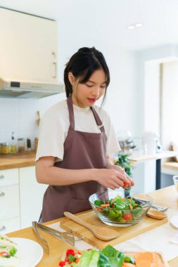 Asyalı kadınlar kahvaltı yemeği ve sebze salatası pişirmek için cam kasede taze sebze hazırlarken aynı zamanda evdeki mutfakta ev yapımı sağlıklı yiyecekler üretiyor..