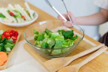 Asyalı kadınlar kahvaltı yemeği ve sebze salatası yapmak için tabakta taze sebze ve kabın içinde marul pişirirken aynı zamanda evde, mutfakta sağlıklı bir yaşam tarzı oluşturuyorlar..