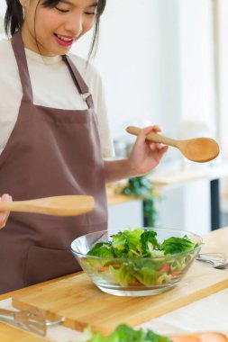 Asyalı kadınlar cam kasede taze sebze ve malzemeyi karıştırmak için tahta kaşık kullanırken kahvaltılık yemek ve sebze salatası pişirirken aynı zamanda ev yapımı sağlıklı yiyecek yaşam tarzı yaratıyorlar..