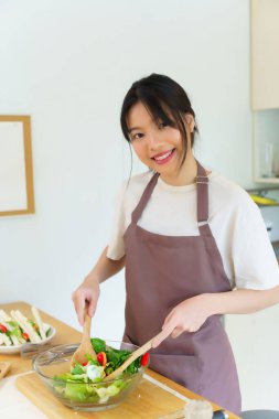 Asyalı kadınlar, cam kasede taze sebzeleri karıştırırken sebze salatası yapmak ve kahvaltı hazırlarken aynı zamanda ev yapımı sağlıklı yiyecekler hazırlıyorlar..