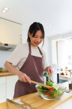 Asyalı kadınlar, cam kasede taze sebzeleri karıştırırken sebze salatası yapmak ve kahvaltı hazırlarken aynı zamanda ev yapımı sağlıklı yiyecekler hazırlıyorlar..