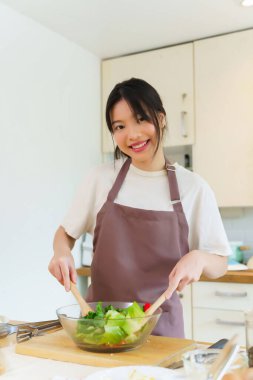 Asyalı kadınlar, cam kasede taze sebzeleri karıştırırken sebze salatası yapmak ve kahvaltı hazırlarken aynı zamanda ev yapımı sağlıklı yiyecekler hazırlıyorlar..