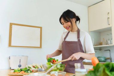 Asyalı kadınlar, cam kasede taze sebzeleri karıştırırken sebze salatası yapmak ve kahvaltı hazırlarken aynı zamanda ev yapımı sağlıklı yiyecekler hazırlıyorlar..