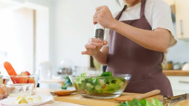 Asyalı kadınlar kahvaltı yemeği ve sebze salatası hazırlamak için malzemeyi karıştırırken aynı zamanda evde, mutfakta ev yapımı sağlıklı yiyecekler yapmak için cam bir kase sebzeye biber ekliyorlar..