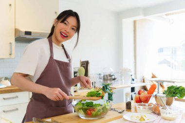 Asyalı kadınlar, cam kasede taze sebzeleri karıştırırken sebze salatası yapmak ve kahvaltı hazırlarken aynı zamanda ev yapımı sağlıklı yiyecekler hazırlıyorlar..