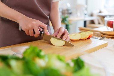 Asyalı kadınların bıçakla tahta kesmek için elmaları keserken kahvaltıda yemek pişirmek için meyve ve taze sebze hazırlarken sağlıklı yiyecek yaşam tarzı hazırlayan elleri..