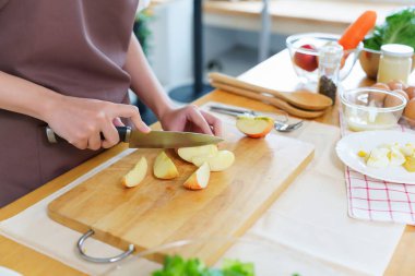 Asyalı kadınların bıçakla tahta kesmek için elmaları keserken kahvaltıda yemek pişirmek için meyve ve taze sebze hazırlarken sağlıklı yiyecek yaşam tarzı hazırlayan elleri..