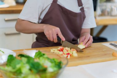 Asyalı kadınların bıçakla panoyu dilimlemek için elma keserken, kahvaltı yemeği ve salata hazırlarken evde sağlıklı bir yaşam sürmelerini sağlamak için meyve hazırlayan elleri..