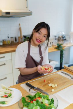 Asyalı kadınlar, kahvaltılık yemek ve salata hazırlamak için taze meyve hazırlarken aynı zamanda mutfakta sağlıklı yiyecek yaşam tarzları hazırlamak için elleriyle tahta keserek elma dilimleri topluyor..