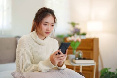 Sörf yapmaktan zevk alan Asyalı genç kadınlar rahat bir kanepede rahatlamak ve evde yavaş bir yaşam tarzıyla vakit geçirmek için etkinlik yaparken akıllı telefonlarıyla sörf yapıyorlar..