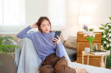 Genç Asyalı süveter giyen kadınlar sosyal medya ve eğlence programlarında sohbet etmek için akıllı telefon kullanırken aynı zamanda koltukta oturup evde yavaş bir yaşam tarzıyla vakit geçirmek için etkinlik yapıyorlar..