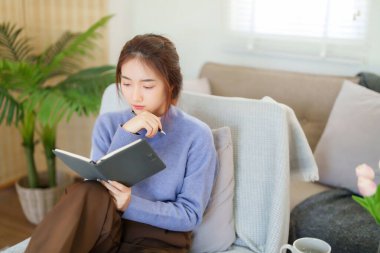 Kazaklı genç Asyalı kadınlar kanepede oturup kitap okumak ve bilgi eğitimi hakkında bilgi sahibi olmak için eğilirken aynı zamanda evde yavaş bir yaşam tarzıyla zaman geçirmek için etkinlik yapıyorlar..