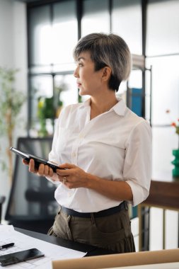 Bir kadın mimar, tasarım kitapları ve materyallerle dolu modern bir ofiste fikirlerini sunmak için özenle bir tablet tutuyor..