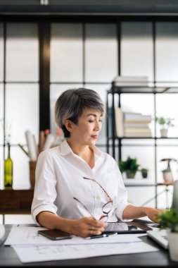 Dişi bir mimar, elinde kalemle masasının planlarını incelerken, iyi organize edilmiş bir çalışma alanına dizayn edilmiş materyallerle derin düşüncelere dalmıştır..