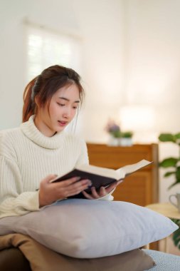 Kazaklı genç Asyalı kadınlar rahat bir kanepede oturup rahatlarken edebiyat kitapları okuyarak ve evde yavaş bir yaşam tarzıyla vakit geçirmek için etkinlik yaparak eğleniyorlar..