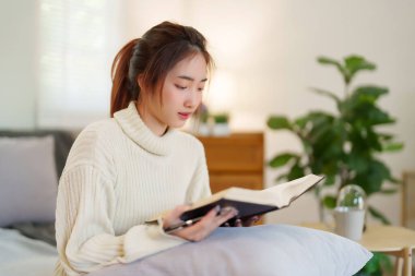 Kazaklı genç Asyalı kadınlar rahat bir kanepede oturup rahatlarken edebiyat kitapları okuyarak ve evde yavaş bir yaşam tarzıyla vakit geçirmek için etkinlik yaparak eğleniyorlar..