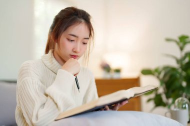 Rahat bir kanepede oturan genç Asyalı kadınlar rahatlarken düşünmek ve öğrenmek için kitap okuyorlar ve evde yavaş yaşam tarzıyla zaman geçirmek için aktivite yapıyorlar..