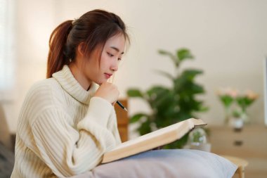 Rahat bir kanepede oturan genç Asyalı kadınlar rahatlarken düşünmek ve öğrenmek için kitap okuyorlar ve evde yavaş yaşam tarzıyla zaman geçirmek için aktivite yapıyorlar..