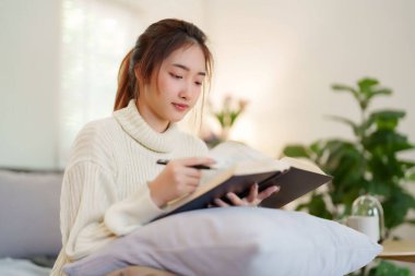 Hırkalı genç Asyalı kadınlar, evde yavaş bir yaşam tarzıyla vakit geçirmek ve rahatlamak için bilgi yazma ve aktivite yapma konusunda kitap okuyup öğrenmek için kitap okuyorlar..