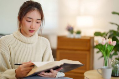 Hırkalı genç Asyalı kadınlar, evde yavaş bir yaşam tarzıyla vakit geçirmek ve rahatlamak için bilgi yazma ve aktivite yapma konusunda kitap okuyup öğrenmek için kitap okuyorlar..