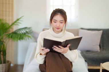 Kazaklı genç Asyalı kadınlar bilgi ve eğitimi öğrenmek için kitap okurken, aynı zamanda kanepede rahatlamak ve evde yavaş bir yaşam tarzıyla zaman geçirmek için etkinlik düzenliyorlar..