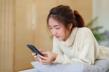 Kazaklı genç Asyalı kadınlar rahat bir kanepede uzanıp rahatlarken akıllı telefondan sosyal medyayla sohbet etmekten ve evde yavaş bir yaşam tarzıyla vakit geçirmekten zevk alıyorlar..