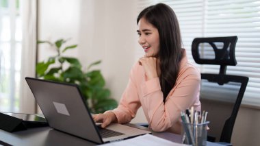 Genç bir kadın ofisinde masasında oturuyor, dizüstü bilgisayarı üzerinde çalışıyor. Odaklanmış ve meşgul görünüyor, yanında bir kahve fincanı ve ofis belgeleriyle, parlak, modern bir çalışma alanında..