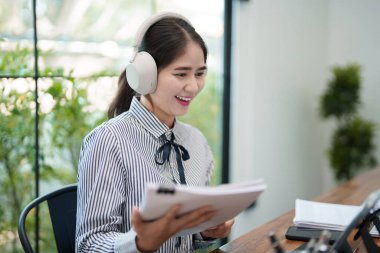 Genç bir kadın gülümsüyor ve elinde bir tabletle kulaklık takıyor, video görüşmesine katılıyor. O, parlak bir ofiste masasında oturuyor.
