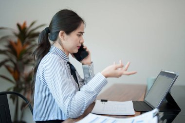 Genç bir kadın masasında oturuyor, eliyle el kol hareketi yaparken telefonla konuşuyor. Önemli bir şeyi tartışıyor gibi görünüyor.
