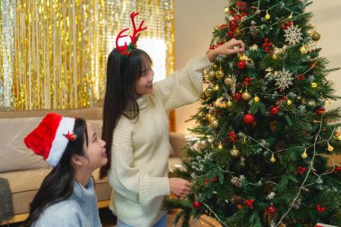 İki arkadaş bir Noel ağacını süslediler, gülümsüyorlar ve Noel Baba şapkaları ve süslemelerle eğleniyorlar..