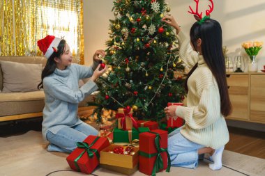 İki arkadaş, hediye kutularıyla çevrili bir Noel ağacını süslemekten mutluluk duyarlar. Bayram ruhu şenlikli, ışıltılı bir arka planla güçlenir.