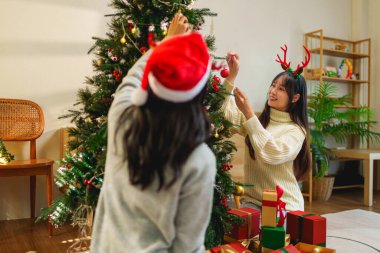 İki arkadaş, hediye kutularıyla çevrili bir Noel ağacını süslemekten mutluluk duyarlar. Bayram ruhu şenlikli, ışıltılı bir arka planla güçlenir.