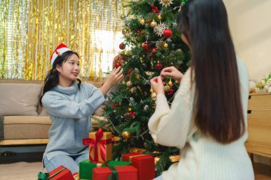 İki arkadaş, hediye kutularıyla çevrili bir Noel ağacını süslemekten mutluluk duyarlar. Bayram ruhu şenlikli, ışıltılı bir arka planla güçlenir.