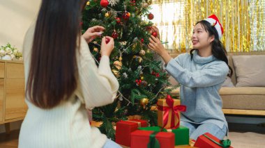 İki arkadaş, hediye kutularıyla çevrili bir Noel ağacını süslemekten mutluluk duyarlar. Bayram ruhu şenlikli, ışıltılı bir arka planla güçlenir.