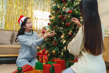 İki arkadaş, hediye kutularıyla çevrili bir Noel ağacını süslemekten mutluluk duyarlar. Bayram ruhu şenlikli, ışıltılı bir arka planla güçlenir.