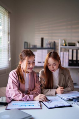 Bir ofis incelemesinde iki iş kadını birlikte gülümseyen ve odaklanan, resmi bir iş ortamında takım çalışmasını ve üretken işbirliğini temsil eden belgeler.