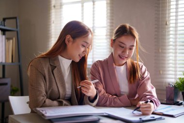 Bir ofis incelemesinde iki iş kadını birlikte gülümseyen ve odaklanan, resmi bir iş ortamında takım çalışmasını ve üretken işbirliğini temsil eden belgeler.