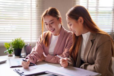 Bir ofis incelemesinde iki iş kadını birlikte gülümseyen ve odaklanan, resmi bir iş ortamında takım çalışmasını ve üretken işbirliğini temsil eden belgeler.