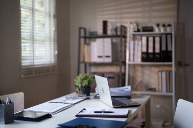 Dizüstü bilgisayarı, belgeleri ve küçük bir saksı bitkisi olan organize bir ofis masası rafların ve pencere perdelerinin arkasına kurulmuş..