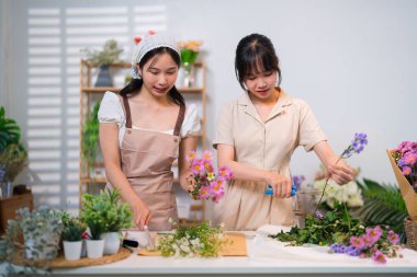 İki çiçekçi neşeli bir anı paylaşırken canlı ve renkli çiçeklerle dolu bir çalışma alanında çiçekler düzenliyorlar..