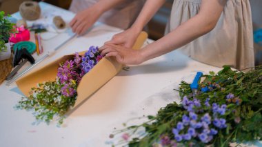 İki çiçekçi, parlak bir dükkanda saksı bitkileri ve renkli çiçeklerle çevrili güzel bir çiçek aranjmanı yapmaya odaklanmış..