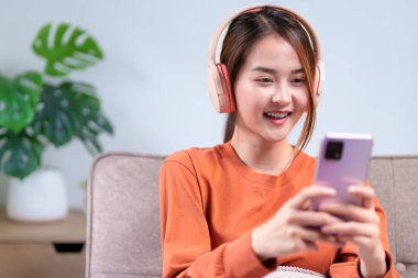 Kulaklık takan, akıllı telefonunu kullanırken gülümseyen genç bir kadın, meşgul edici bir cep telefonu deneyimine daldı..